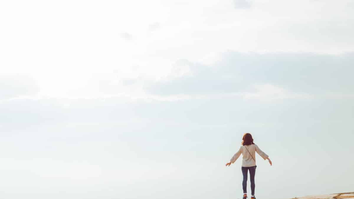 A woman standing on a hilltop embracing the open sky with a sense of freedom.