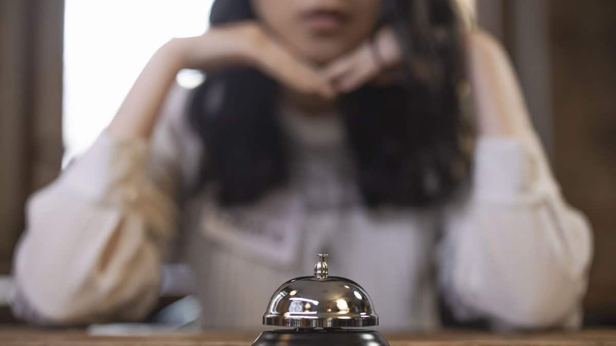 Reception bell on a wooden table with a blurred person in the background, creating focus on hospitality service.
