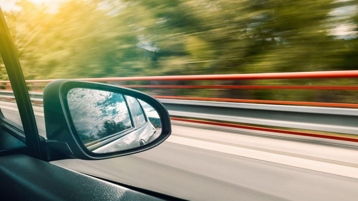 Side mirror view capturing high-speed travel on an expressway with motion blur effect.