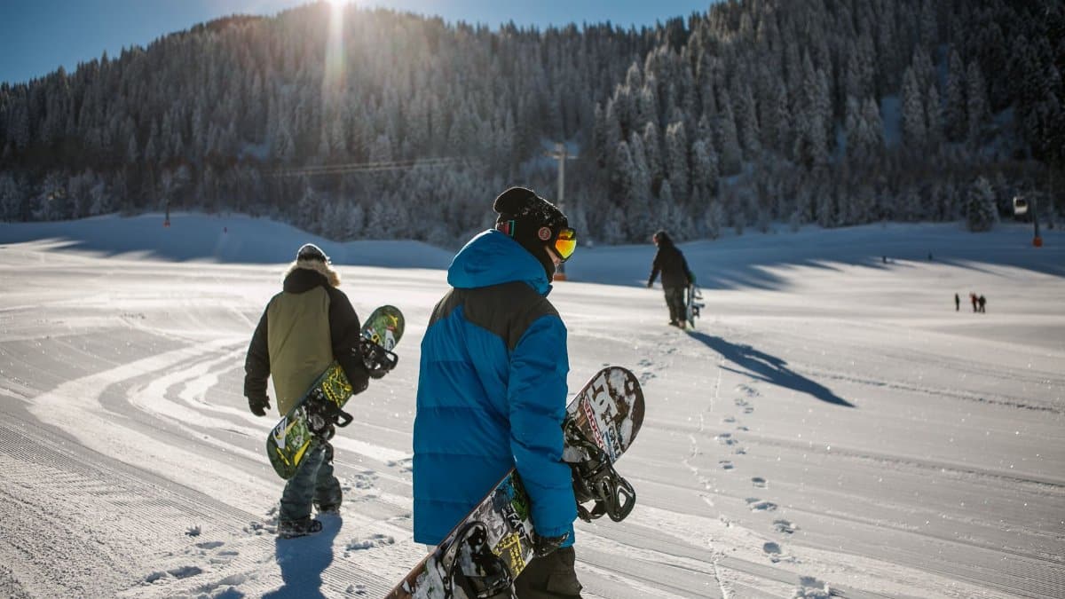 Group of snowboarders walking up a snowy ski slope during a sunny winter day in the mountains.