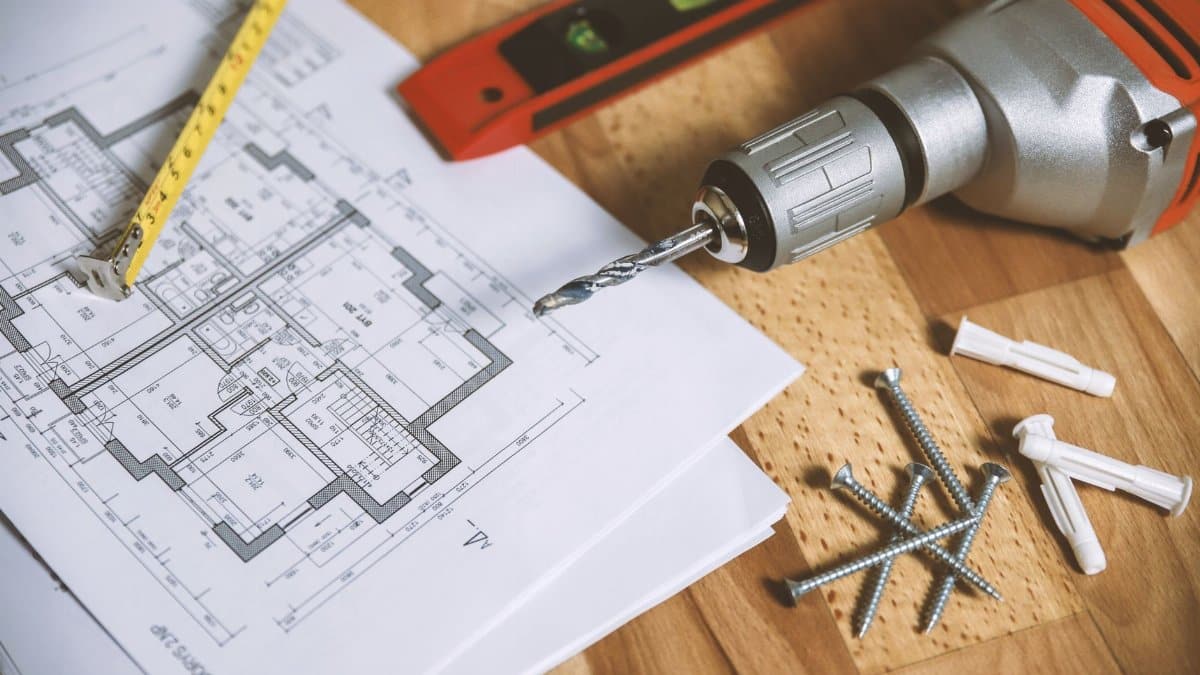 Close-up of construction blueprint with tools like drill and screws on a wooden table.
