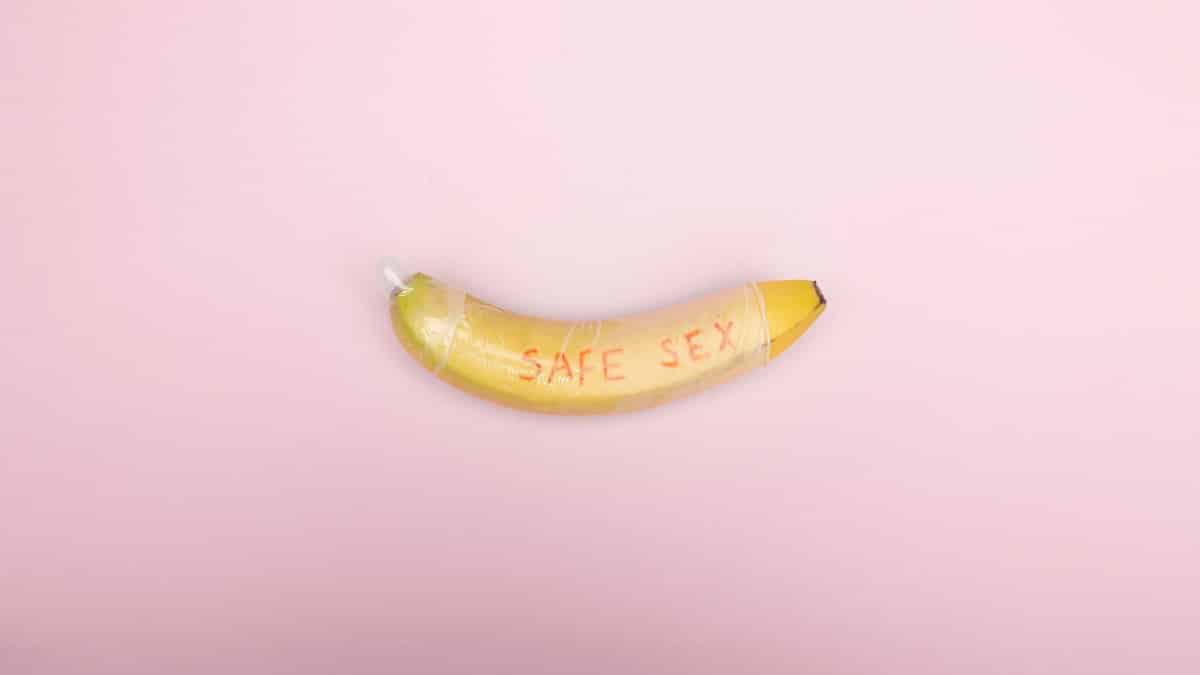 Still life image of a banana wrapped in a condom with 'safe sex' text on a pink background.