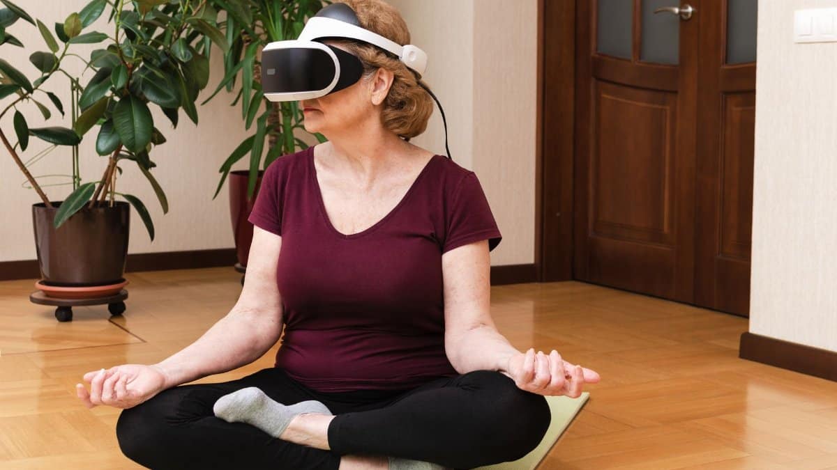 A senior woman practices meditation using VR headset indoors, blending fitness and technology.