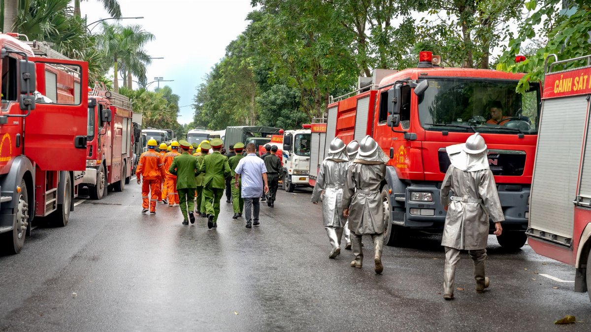 Firefighters in uniforms and fire trucks responding to an emergency on a city street with lush greenery.