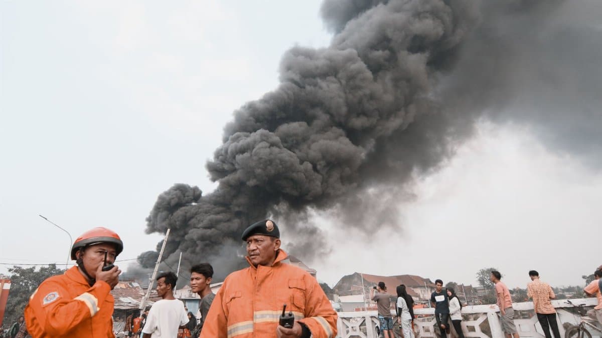 Firefighters in protective suits managing a chaotic situation with heavy smoke in the background. Emergency response underway.
