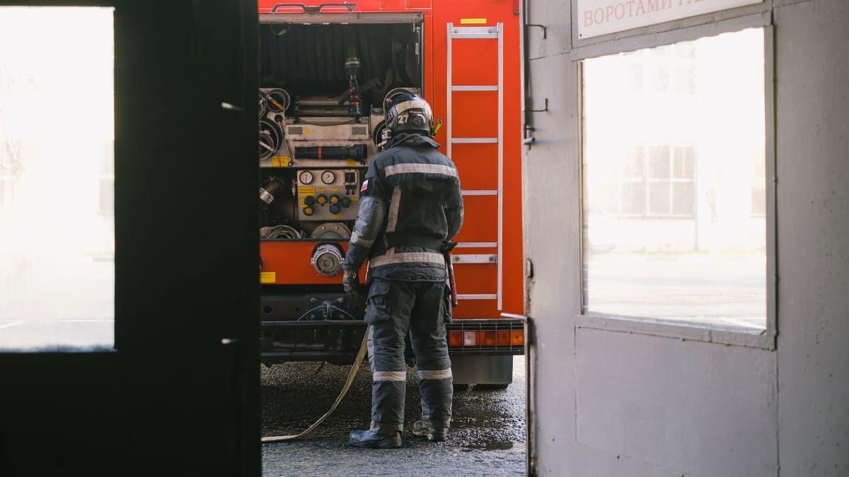 Firefighter preparing equipment at fire engine near station entrance. Safety and emergency readiness.