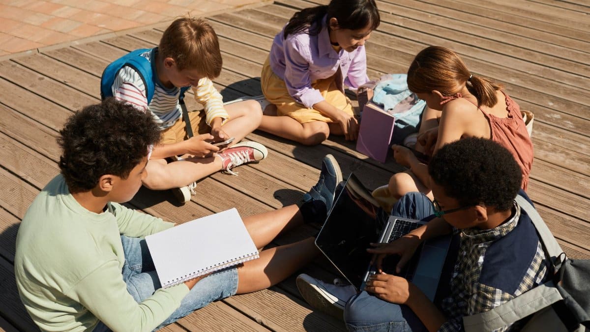Group of diverse teenagers collaborating outdoors using laptop and notebooks.