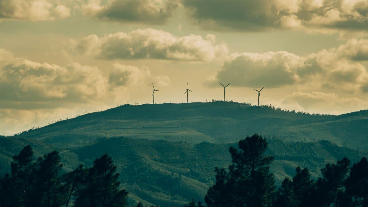 Wind turbines on a hill under a dramatic cloudy sky, showcasing renewable energy amidst nature.