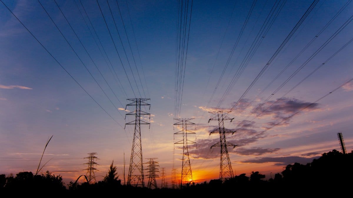Silhouette of transmission towers against a colorful sunset sky with power lines stretching across the horizon.
