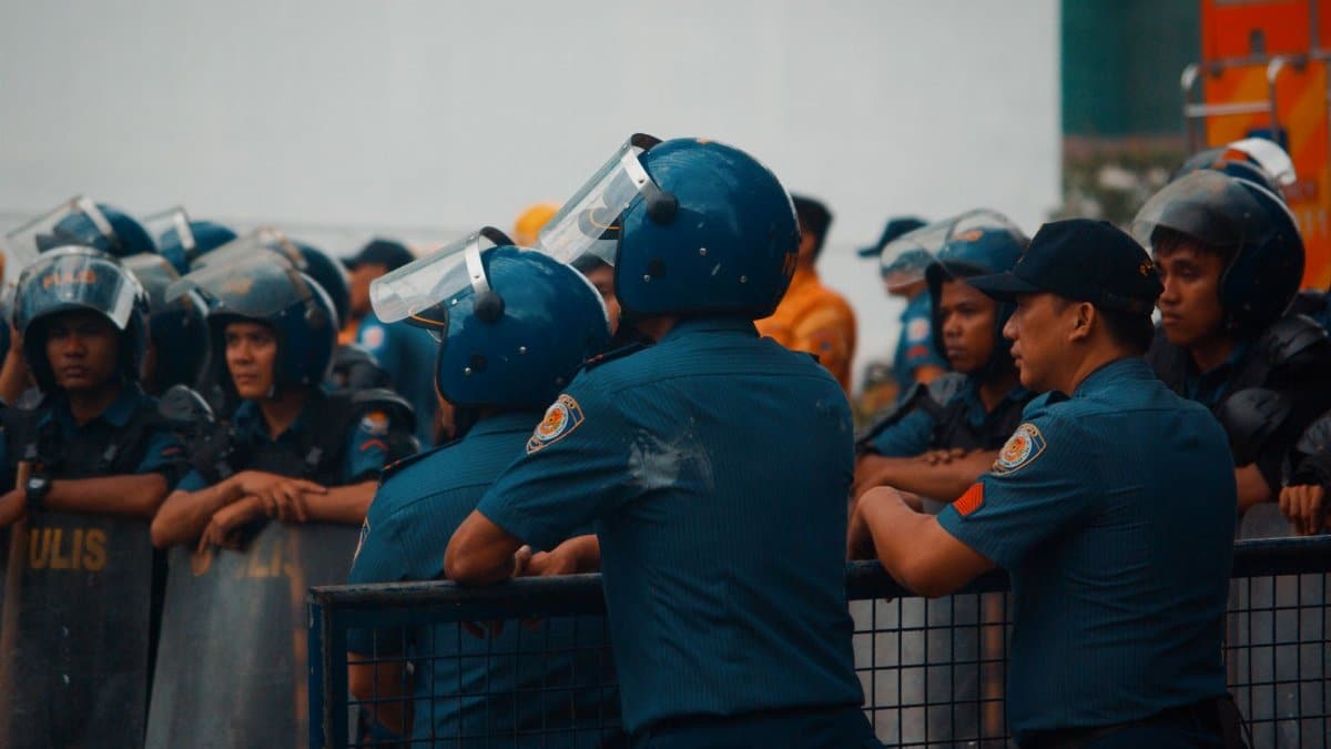 Group of police officers wearing riot gear during a daytime protest outdoors.