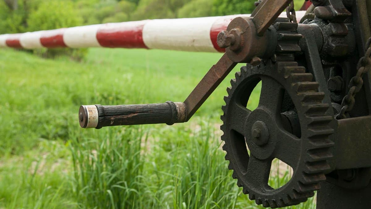 Close-up of a mechanical gear and barrier against a green grassland backdrop.