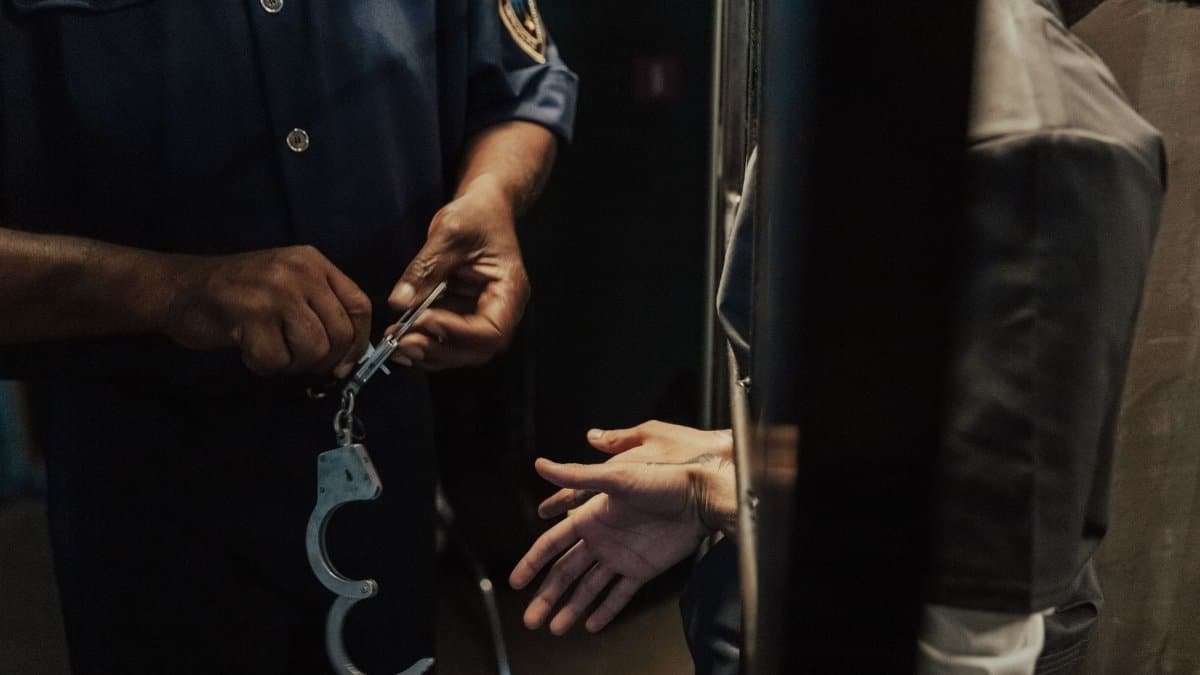 A police officer handcuffing a suspect through bars indoors, signifying arrest and law enforcement.