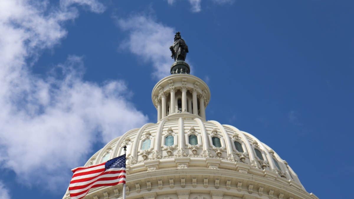 Capture of the U.S. Capitol dome with an American flag waving against a blue sky in Washington, D.C.
