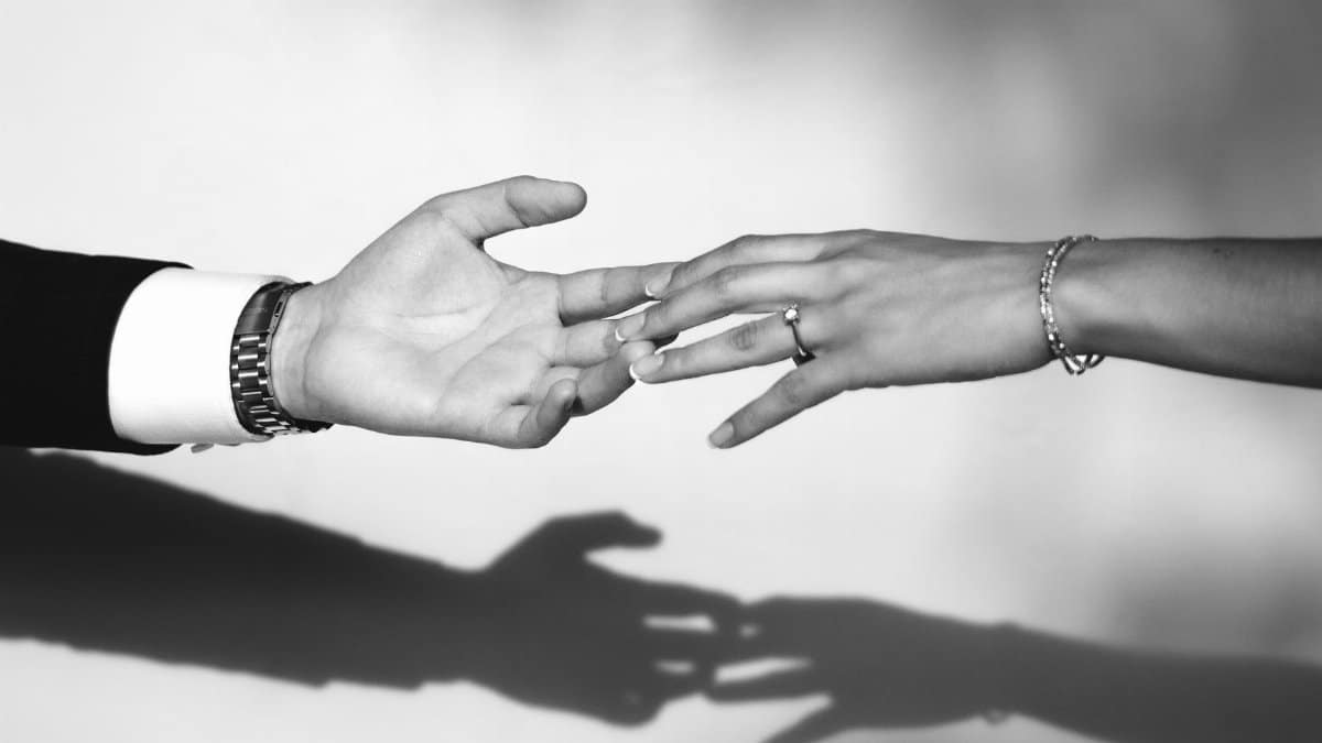 Close-up black and white photo of couple reaching hands with engagement ring and shadows.