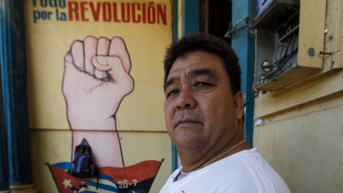 Man standing by a revolutionary mural with a raised fist and Cuban flag emblem.