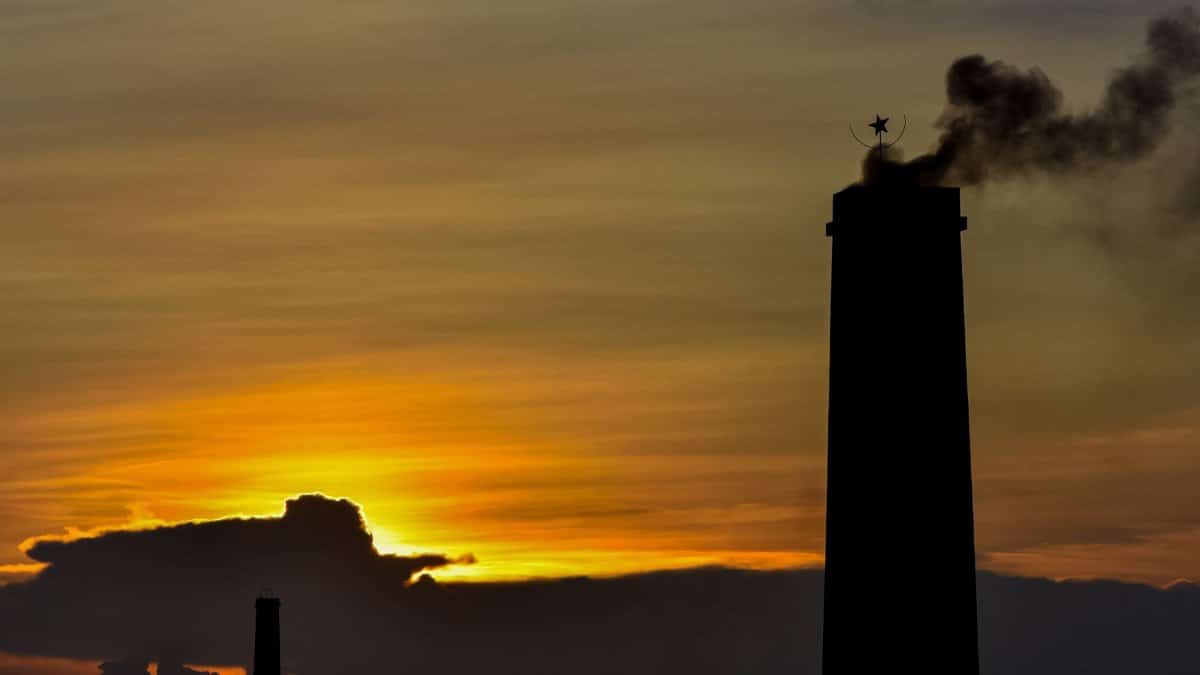 Silhouette of a chimney with smoke against a vibrant sunset sky, showcasing industrial emissions.