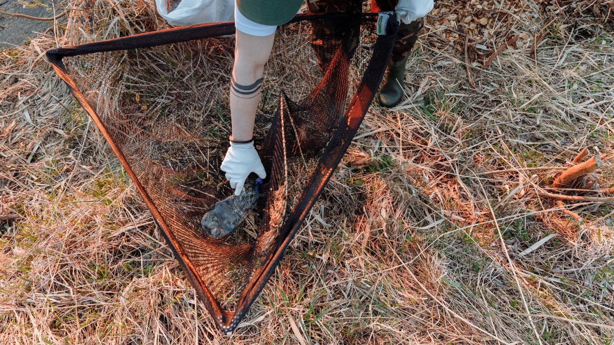 A volunteer cleaning up litter in a grassy area, promoting environmental conservation.