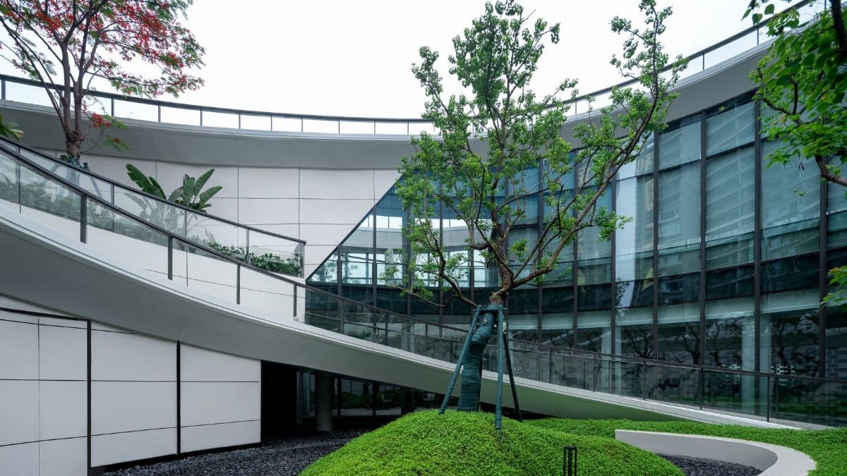 Curved glass building with lush green landscaping and modern design.