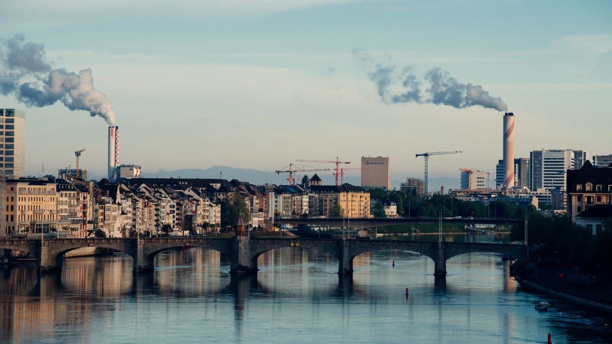 A view of Basel's skyline with the Rhine River reflecting city architecture and smoking chimneys.