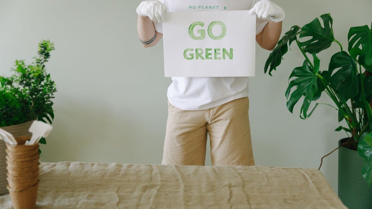A person holding a 'Go Green' sign promoting environmental awareness indoors.