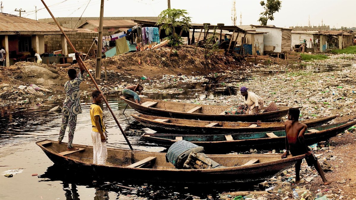 Children and wooden boats on a polluted river in Lagos, Nigeria, depicting everyday life and environmental challenges.