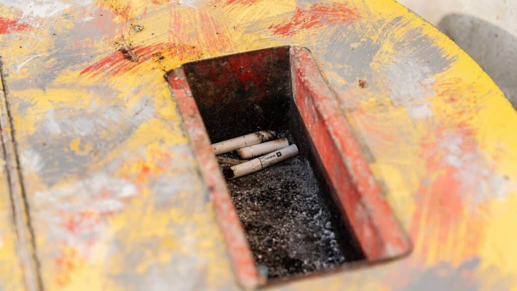 A close-up of a colorful garbage bin filled with cigarette butts.