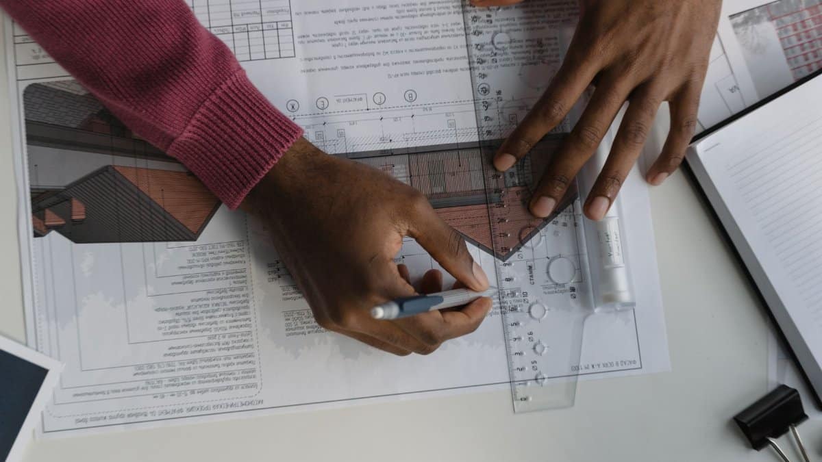 Architect sketching on blueprints with ruler at desk, designing a building layout.