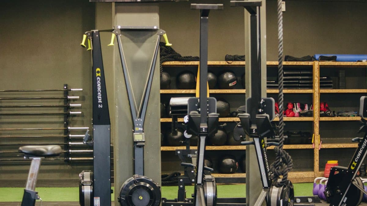 Modern gym with exercise equipment including rowing and ski machines, weights, and ropes.