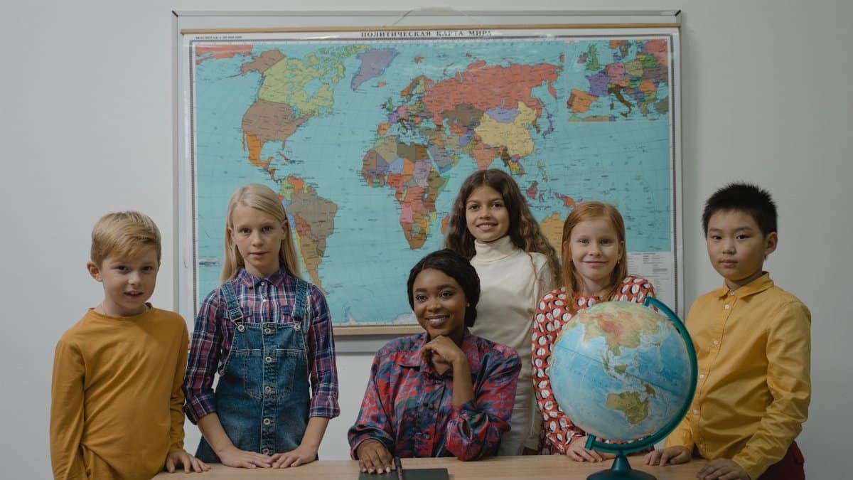 A diverse group of students with a teacher in a classroom setting featuring a globe and world map.