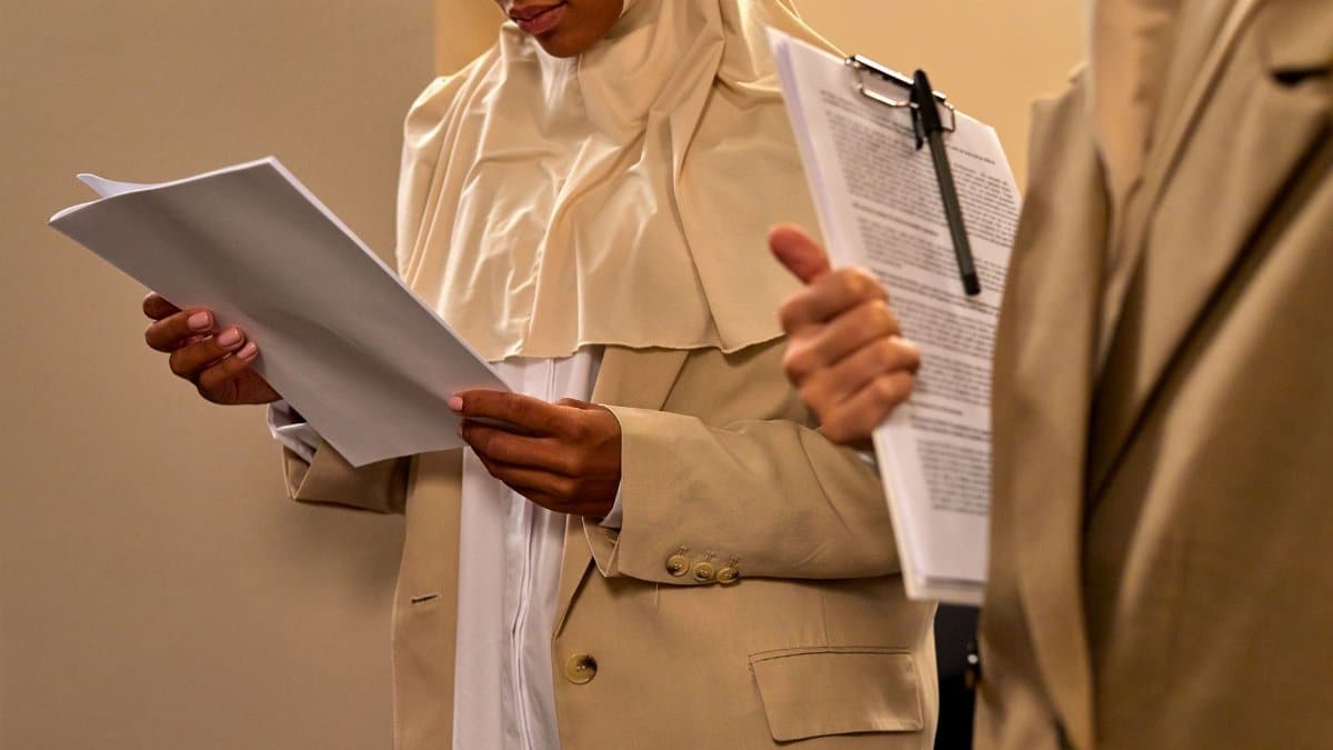 A professional woman in a hijab reviews documents, showcasing focus and diligence.