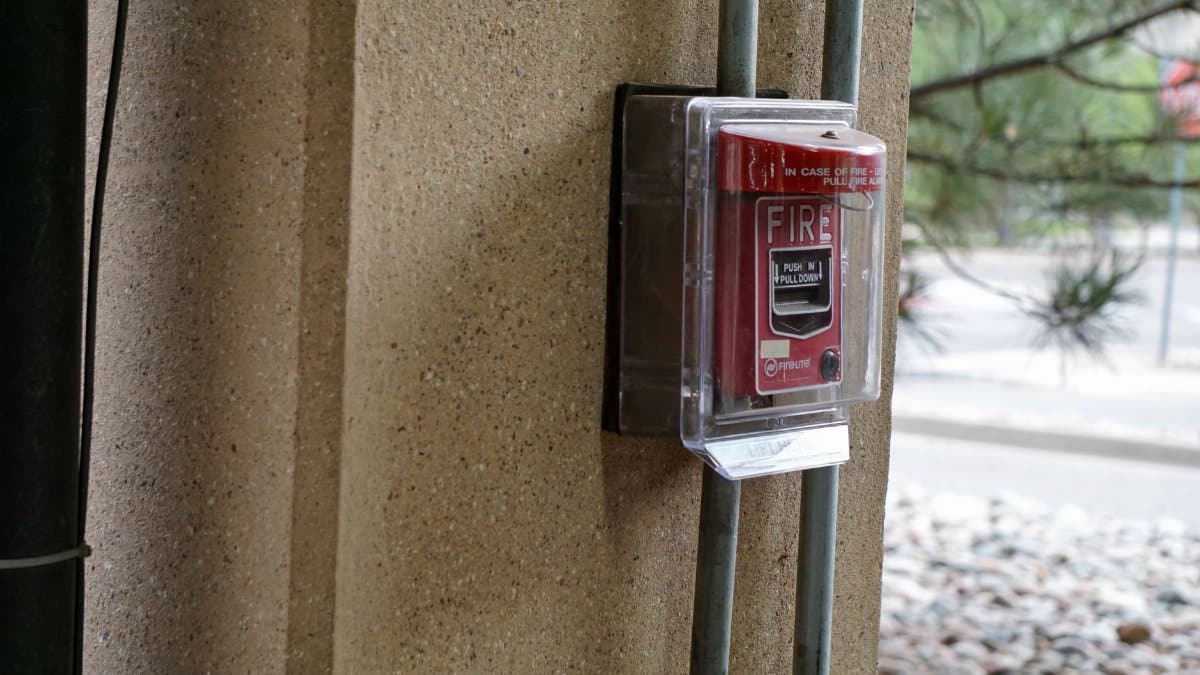 Close-up view of a red fire alarm mounted on a textured outdoor wall, showcasing safety equipment.