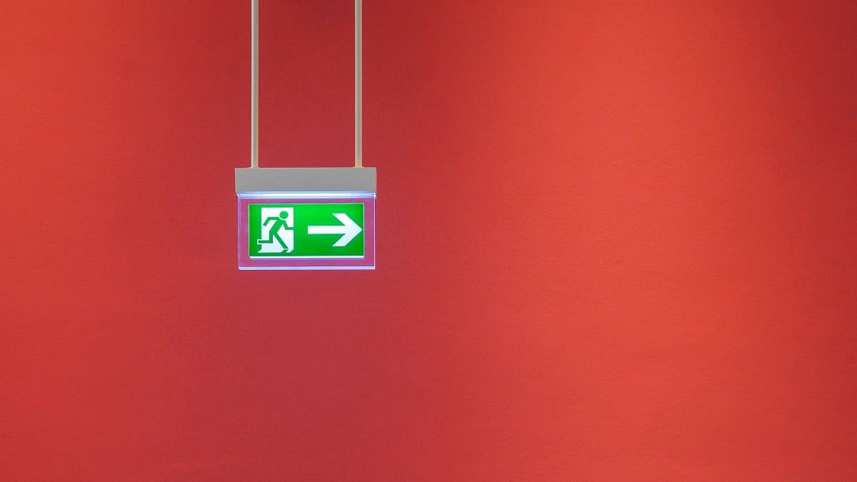 Green emergency exit sign with arrow on vibrant red wall, indicating direction for safety.