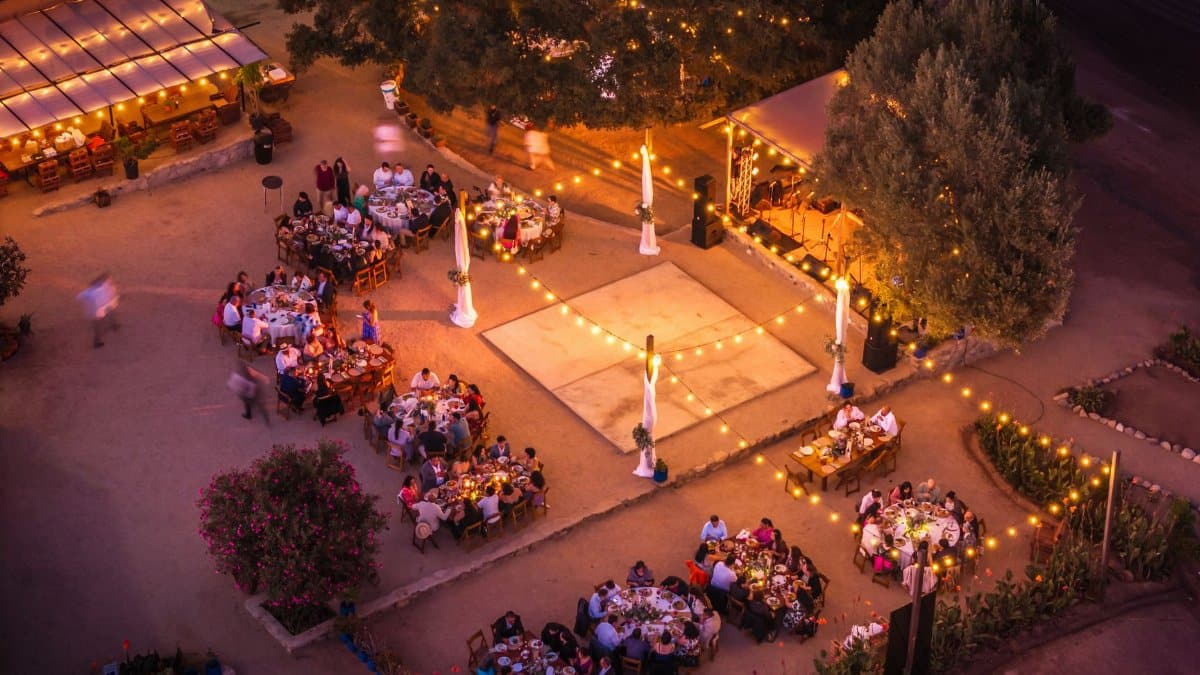 A drone captures a lively outdoor evening party with string lights and decorated tables.