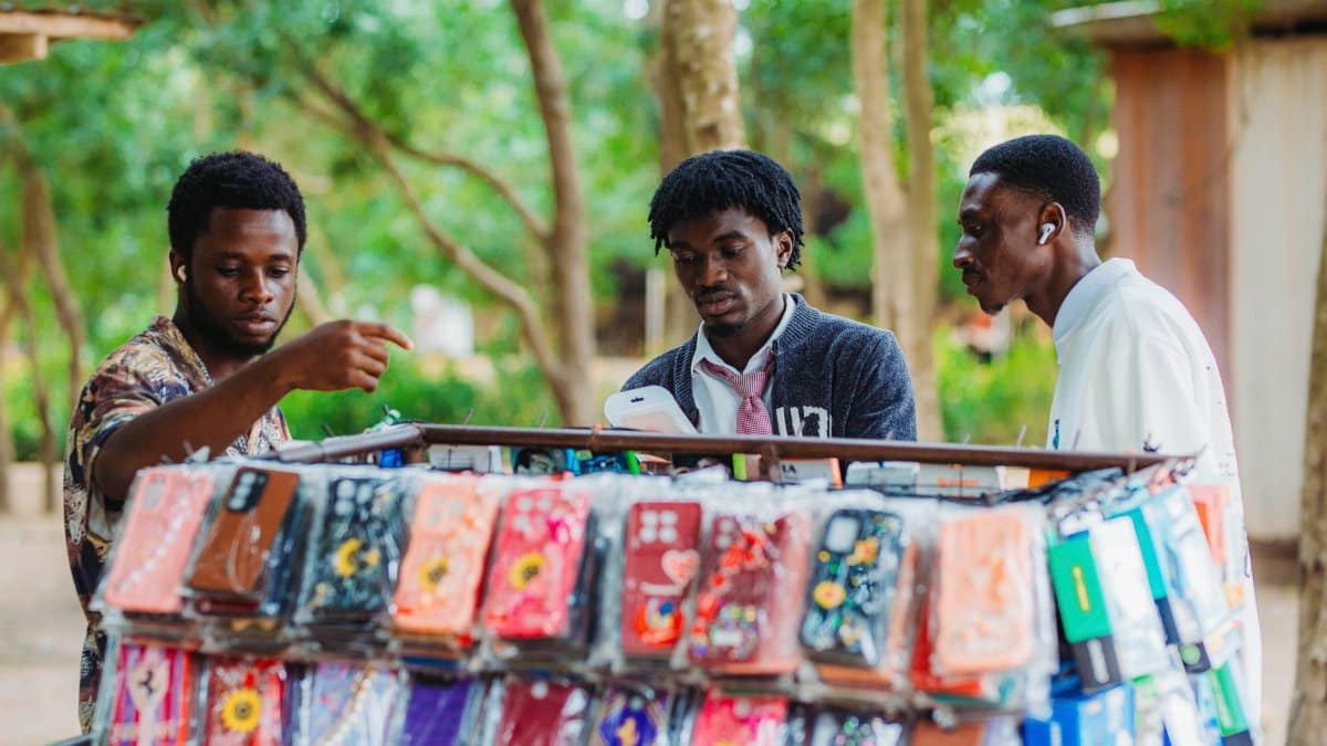 Three men browsing phone cases at an outdoor market stall in Accra, Ghana.