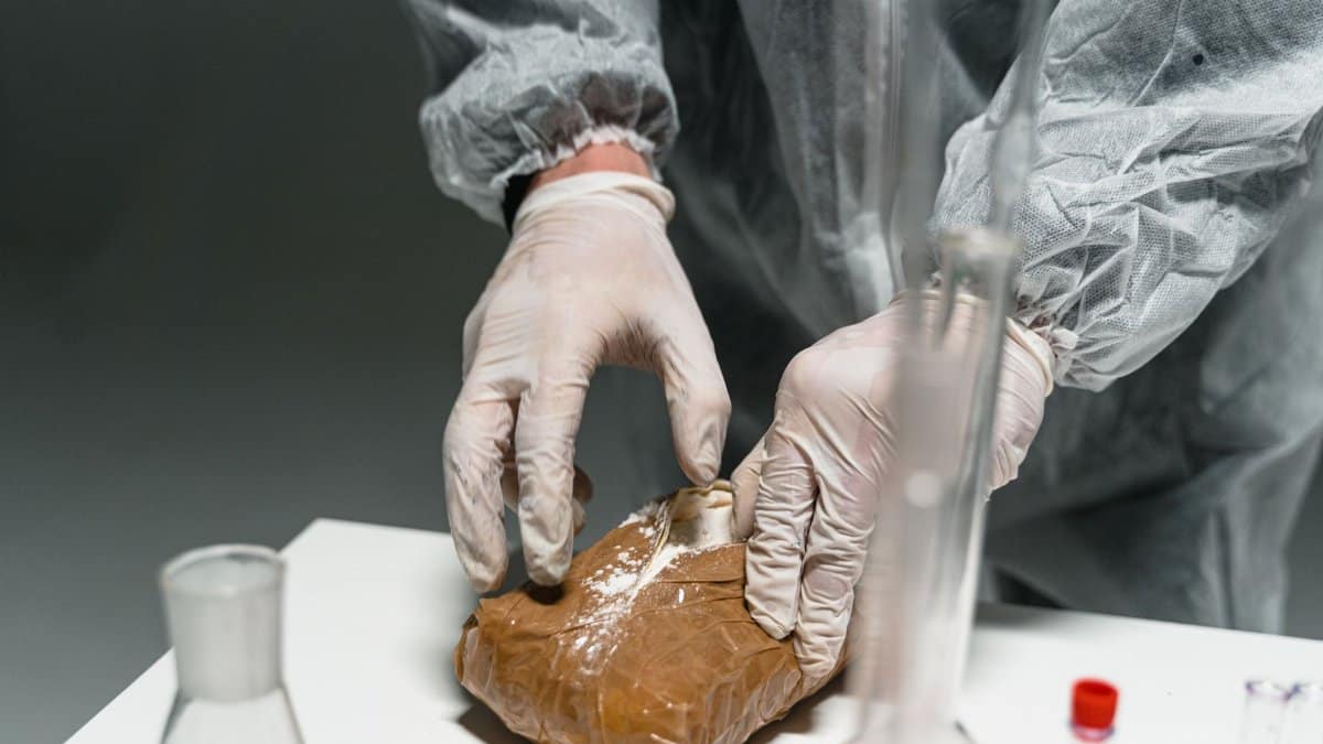 Lab worker analyzes powdered substance in a laboratory setting using safety gear.