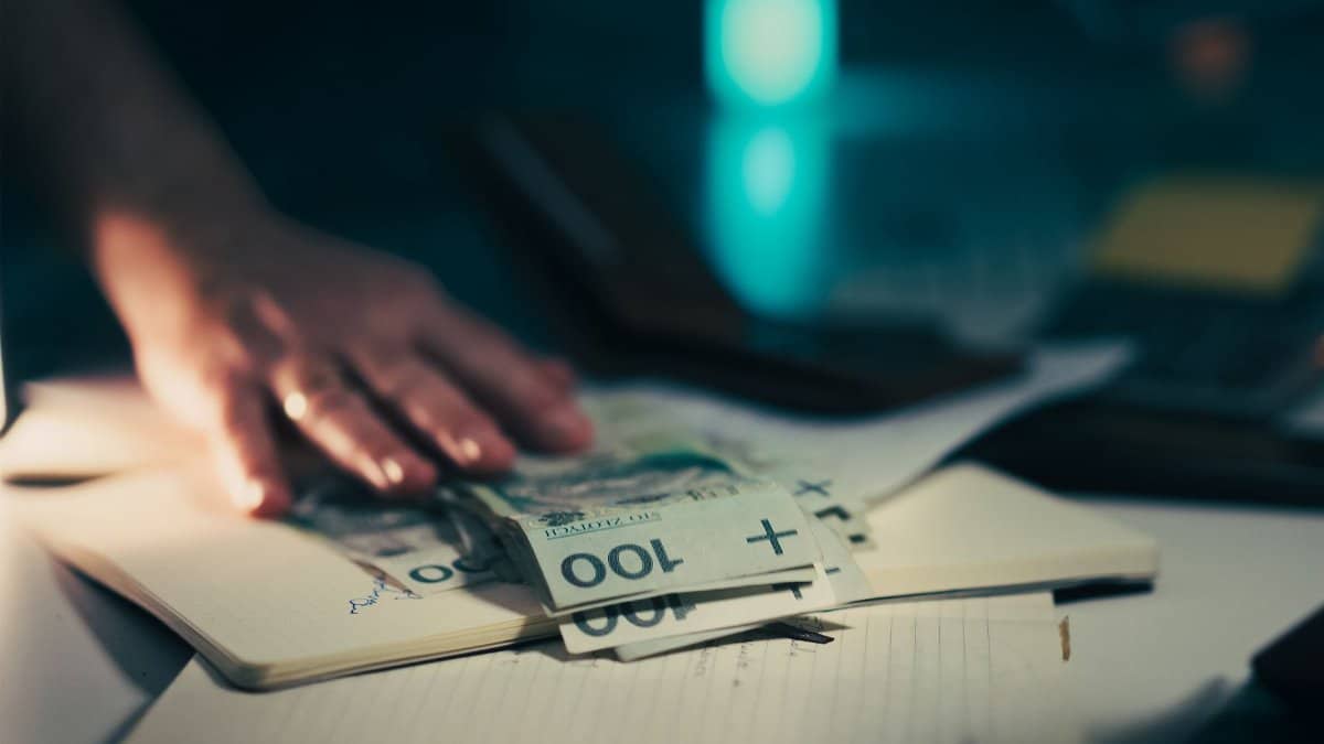Close-up of hand reaching for banknotes on an office desk with a notebook and calculator.