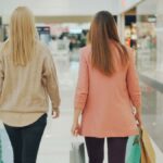 Two women walking in a mall holding shopping bags, back view.