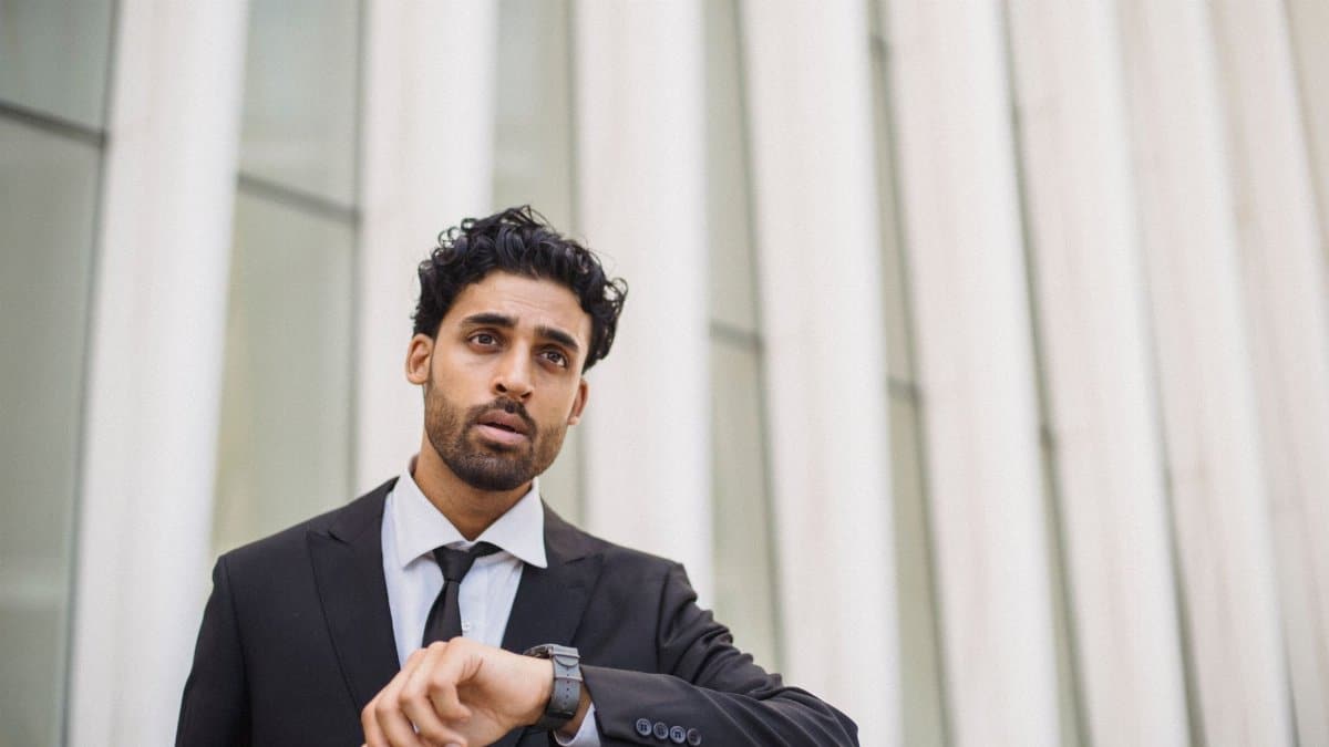 A professional man in a suit checks the time on his watch while standing outside, capturing a business theme.