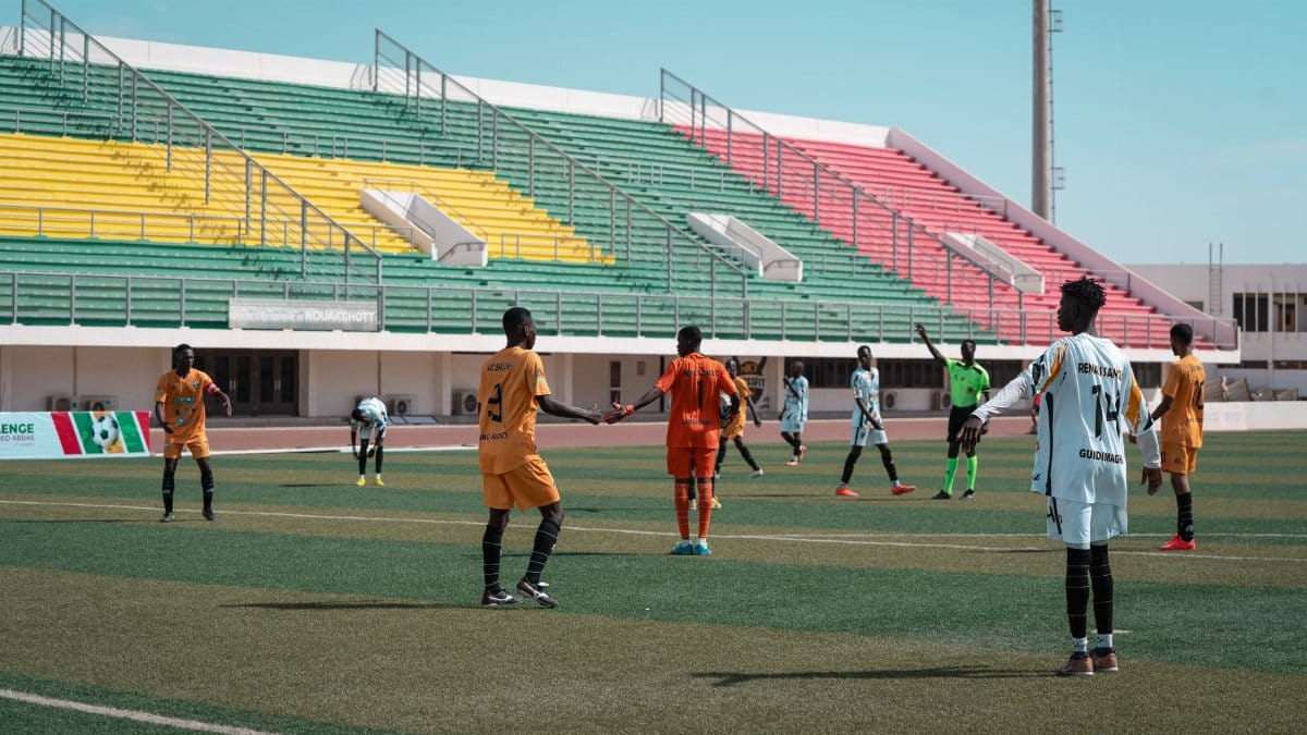 Energetic football match with players in orange and white, vibrant stadium backdrop.