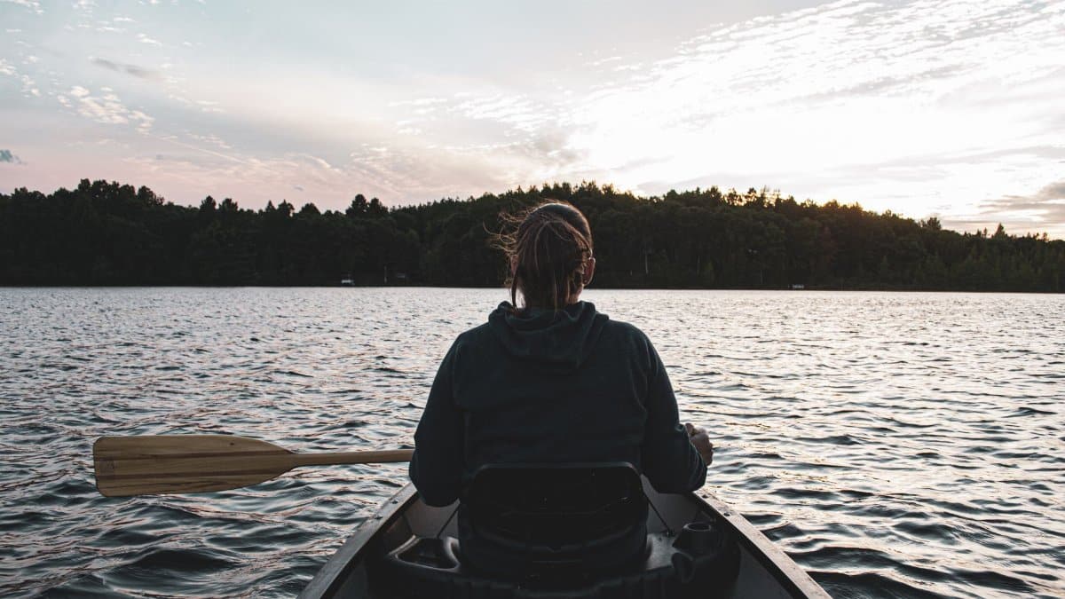 A woman paddles a canoe on a tranquil Minnesota lake at sunset, surrounded by nature.