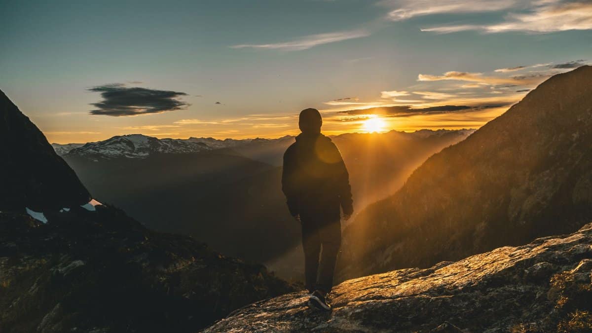 A person stands on a mountain lookout during a breathtaking sunrise, showcasing nature's beauty.