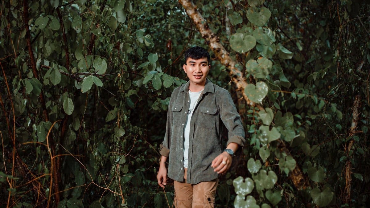 A young man in casual attire exploring a dense, leafy forest during daytime, showcasing adventure and nature.