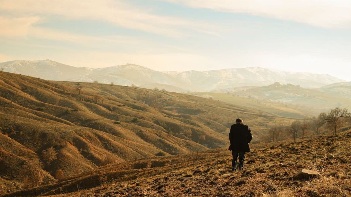 A man walks through a sprawling rural mountain landscape under a serene sky.