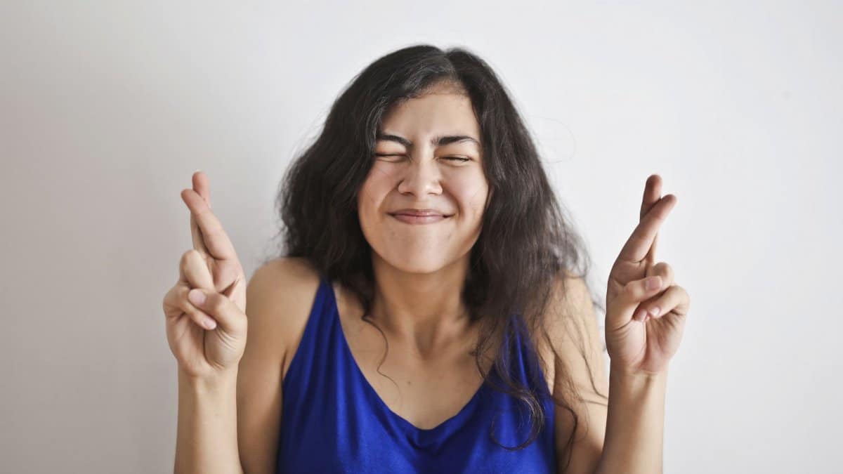 Happy woman with fingers crossed, expressing hope and good luck, on a white background.
