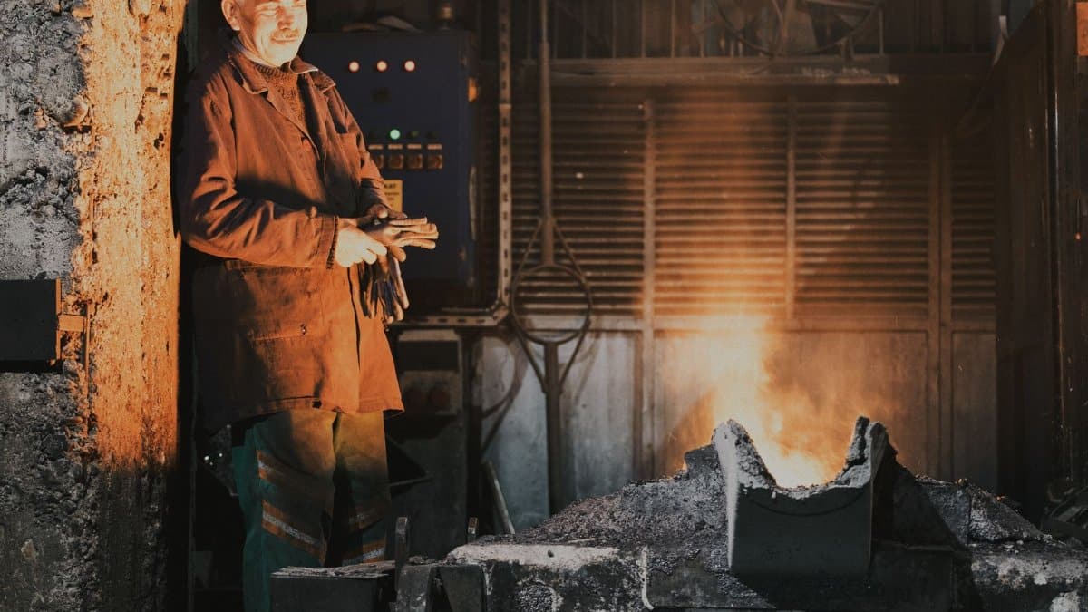 A seasoned worker stands by a furnace in an industrial foundry, casting a warm glow.