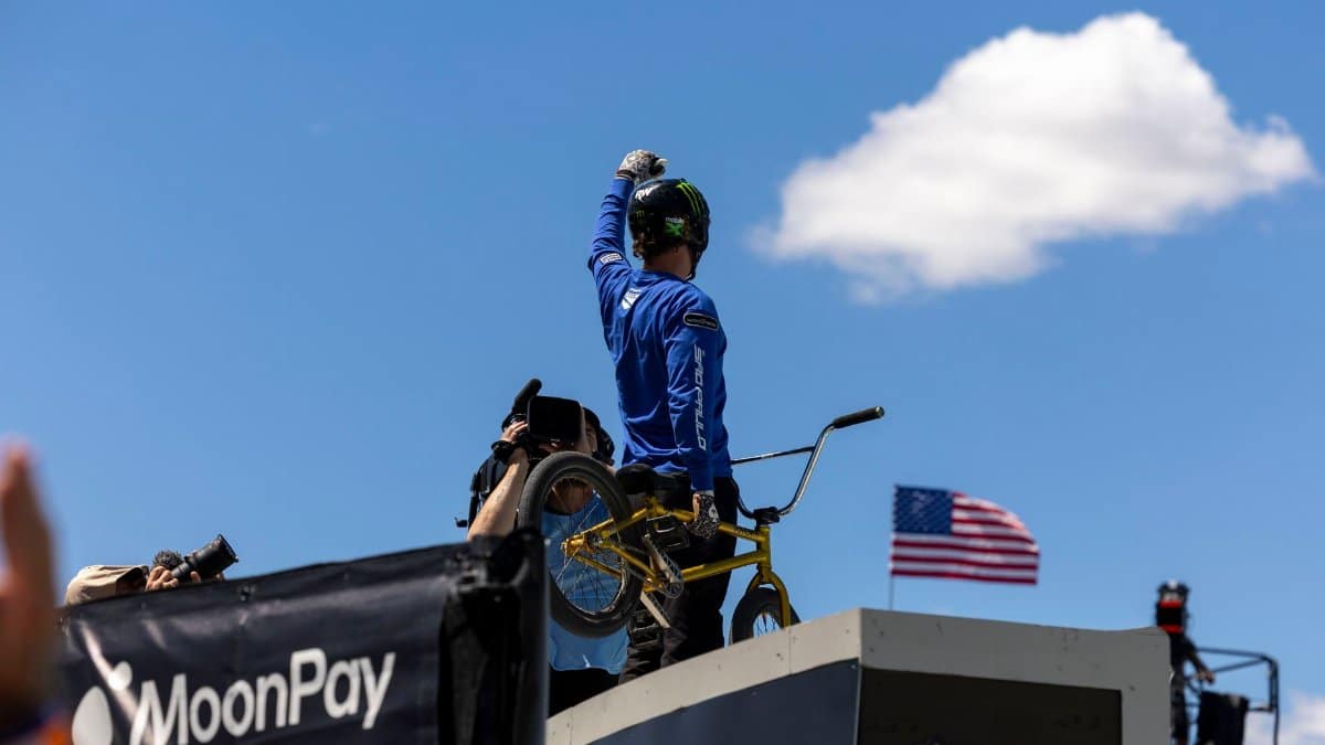 BMX rider celebrates atop ramp with American flag and clear sky, highlighting extreme sports excitement.