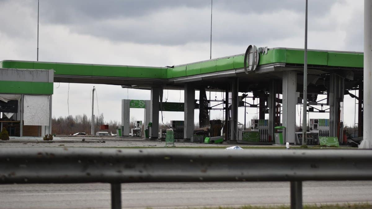 A deserted and damaged gas station shows signs of destruction under a cloudy sky.