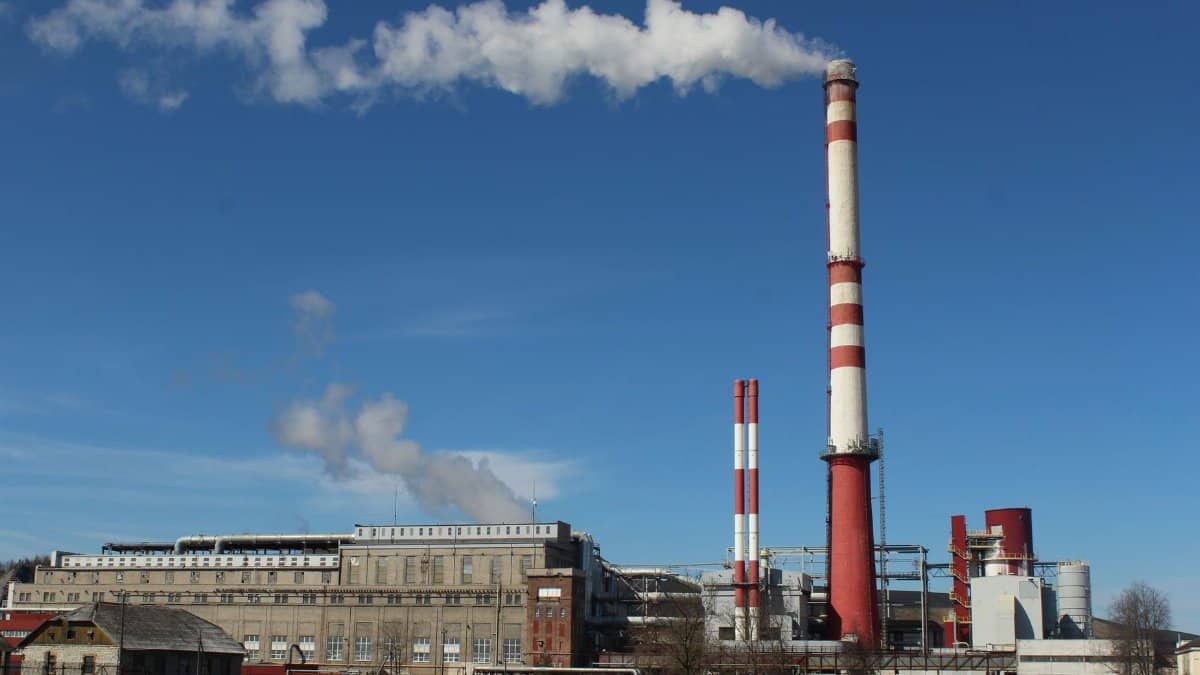 A large industrial factory with tall chimneys emitting smoke under a clear blue sky.
