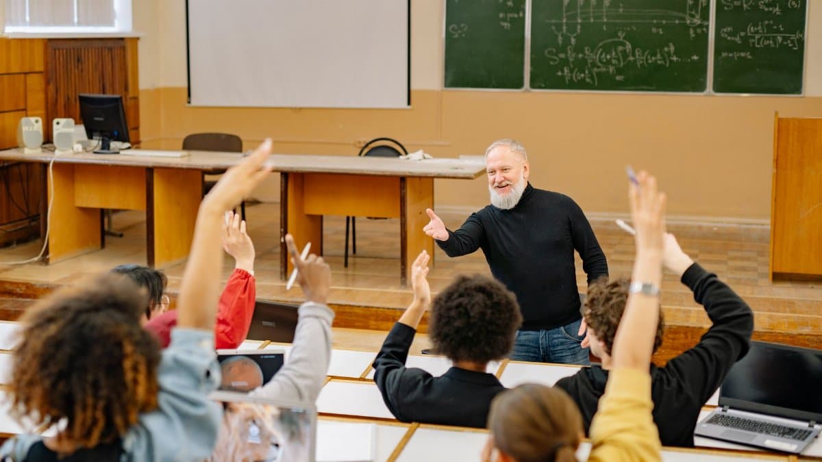 Professor engaging with students in a lively university classroom discussion as students raise hands.