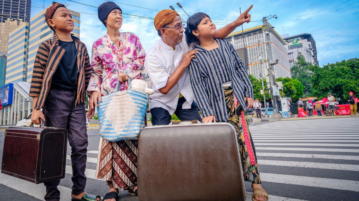 A family in traditional Javanese clothing crosses a street in Jakarta, suggesting a cultural journey.